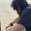 Shashwat Sanatan leaning over a boat rail, a rudraksha mala on his wrist.